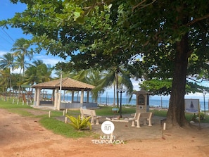 Un pabellón junto a la playa con techo de tejas, rodeado de palmeras y bancos.