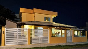 Una casa de dos pisos con techo plano, ventanas grandes y entrada protegida por una reja.