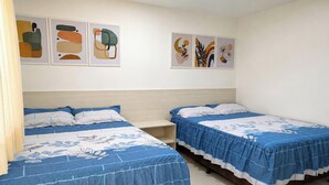 Habitación de hotel con dos camas, cada una con cubrecama azul y almohadas blancas. Se observan obras de arte colgadas en la pared sobre las camas.