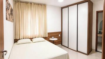 Quarto de hotel com cama, mesa de cabeceira, guarda-roupa e banheiro visível por uma porta aberta.