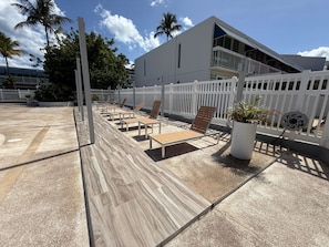 A pool area with lounge chairs, a white fence, and a building with a balcony. - Beachfront, Ocean Views & Renovated Spaces (Dorado)