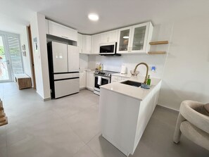 A modern kitchen with white cabinetry, a central island, a microwave, and a sink. - Beachfront, Ocean Views & Renovated Spaces (Dorado)