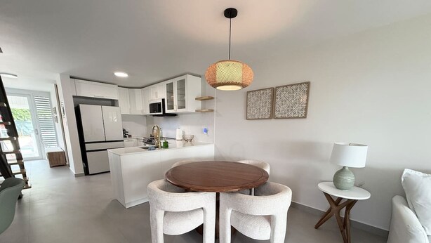 Een moderne keuken met witte kastjes, een eethoek met een ronde tafel en twee stoelen, en een klein bijzettafeltje met een lamp.