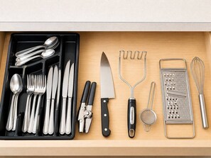 A drawer containing various kitchen utensils including spoons, forks, knives, a grater, a strainer, and a whisk. - Comfortable stay (Kissimmee)