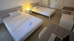 Una camera d'albergo con due letti, una scrivania con un portatile, un armadio e una porta.