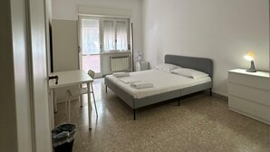 Una camera da letto con un letto, una scrivania, una sedia, un comodino con una lampada e un termosifone.