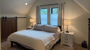A bedroom with a sloped ceiling, a bed with two bedside tables, two lamps, and a window with curtains. - Hungry Horse Farmhouse, 10 minutes to Glacier, Firepit (Hungry Horse)