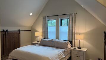 A bedroom with a sloped ceiling, a bed with two bedside tables, two lamps, and a window with curtains.