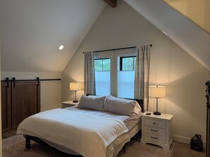 A bedroom with a sloped ceiling, a bed with two bedside tables, two lamps, and a window with curtains. - Hungry Horse Farmhouse, 10 minutes to Glacier, Firepit (Hungry Horse)
