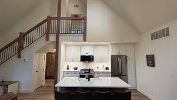 A spacious kitchen with a central island, white cabinetry, and a stainless steel refrigerator.