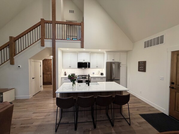 A modern kitchen with white cabinets, stainless steel appliances, and a central island with bar stools. - Hungry Horse Farmhouse, 10 minutes to Glacier, Firepit (Hungry Horse)