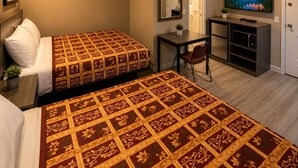 Habitación de hotel con dos camas, un escritorio con silla, televisor y una puerta.
