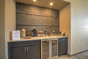 A kitchen area with a stone backsplash, a coffee station, and a sign offering complimentary coffee and water.
