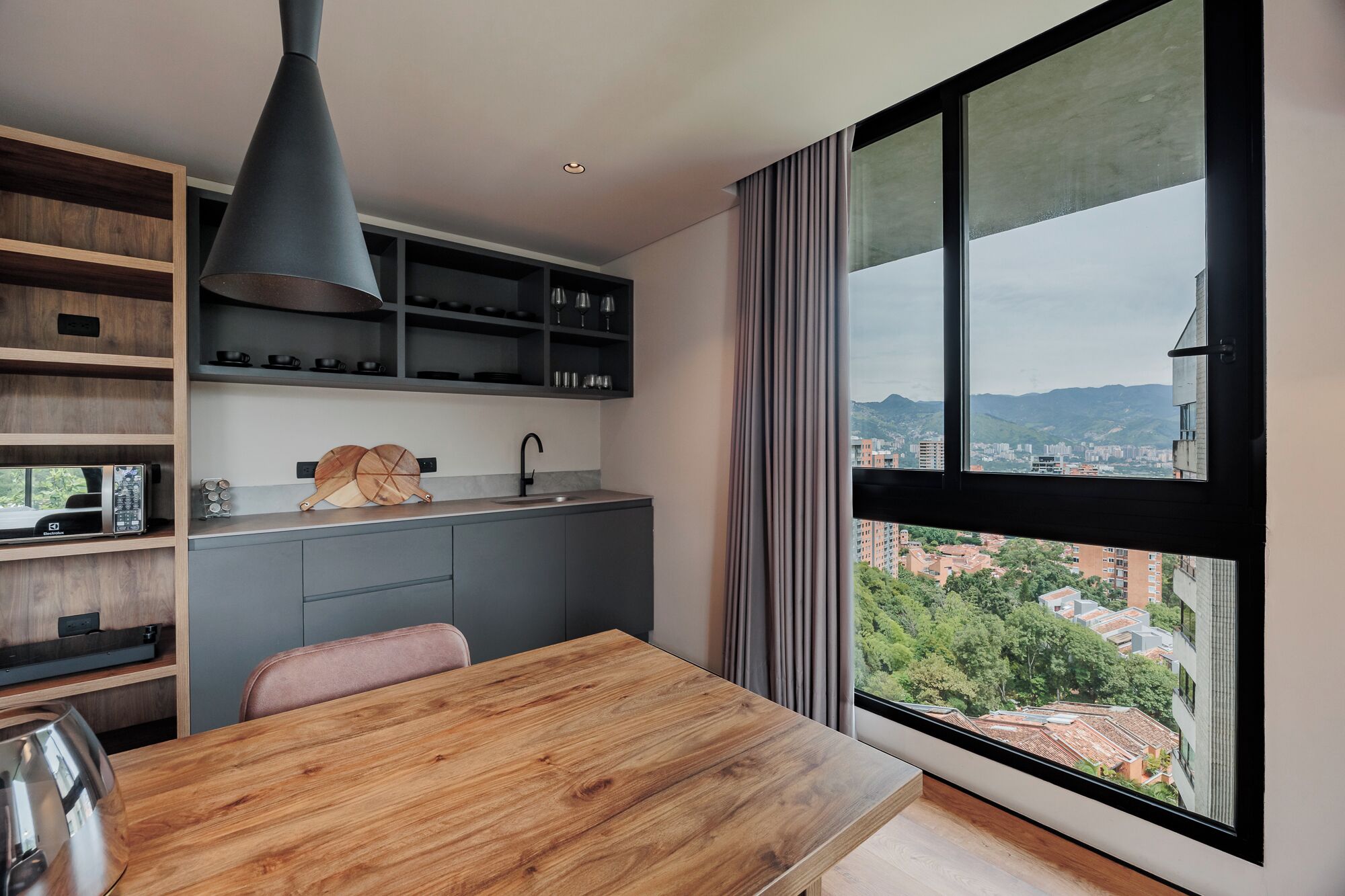 A modern kitchen with a large window, wooden cabinets, and a dining area with a wooden table.