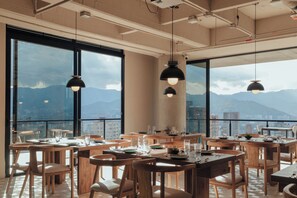 A restaurant with large windows, wooden tables, and hanging pendant lights.