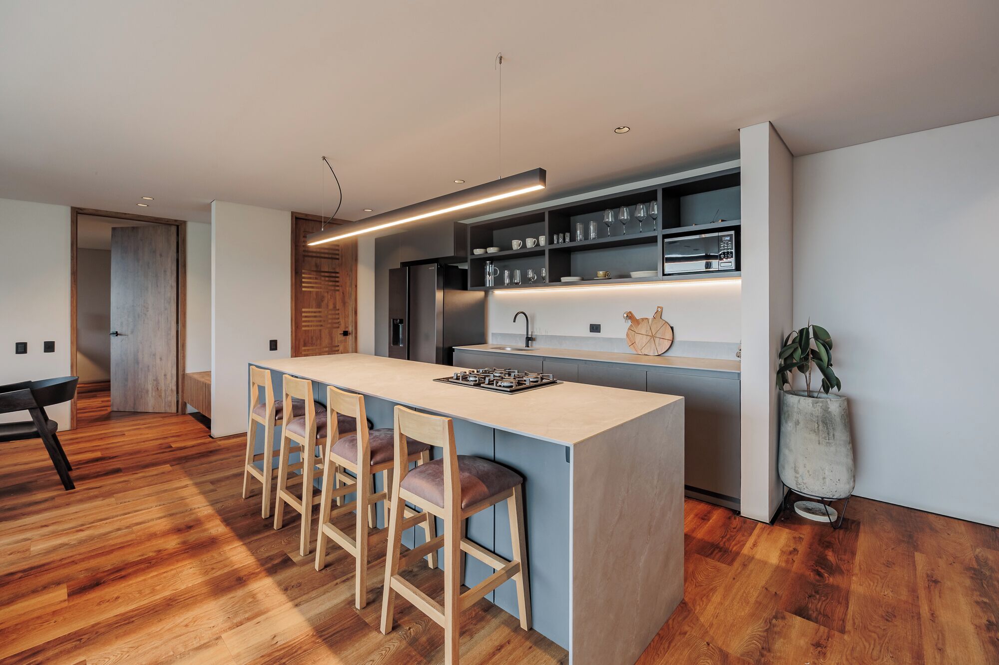 A modern kitchen with a central island, bar stools, a refrigerator, and a built-in oven.