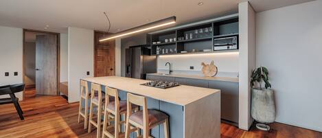 A modern kitchen with a central island, bar stools, a refrigerator, and a built-in oven.