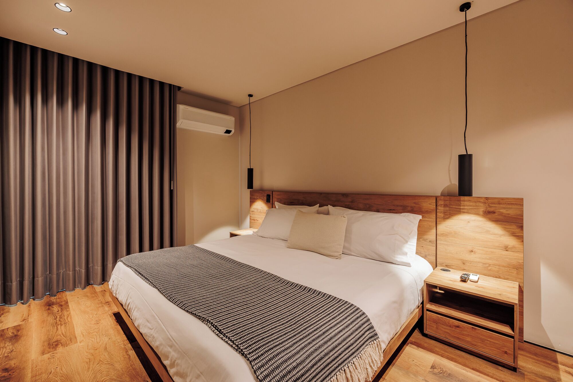Et moderne soveværelse med sengegavl i træ, et sengebord med lampe, og en stor seng med mønstret dyne.
