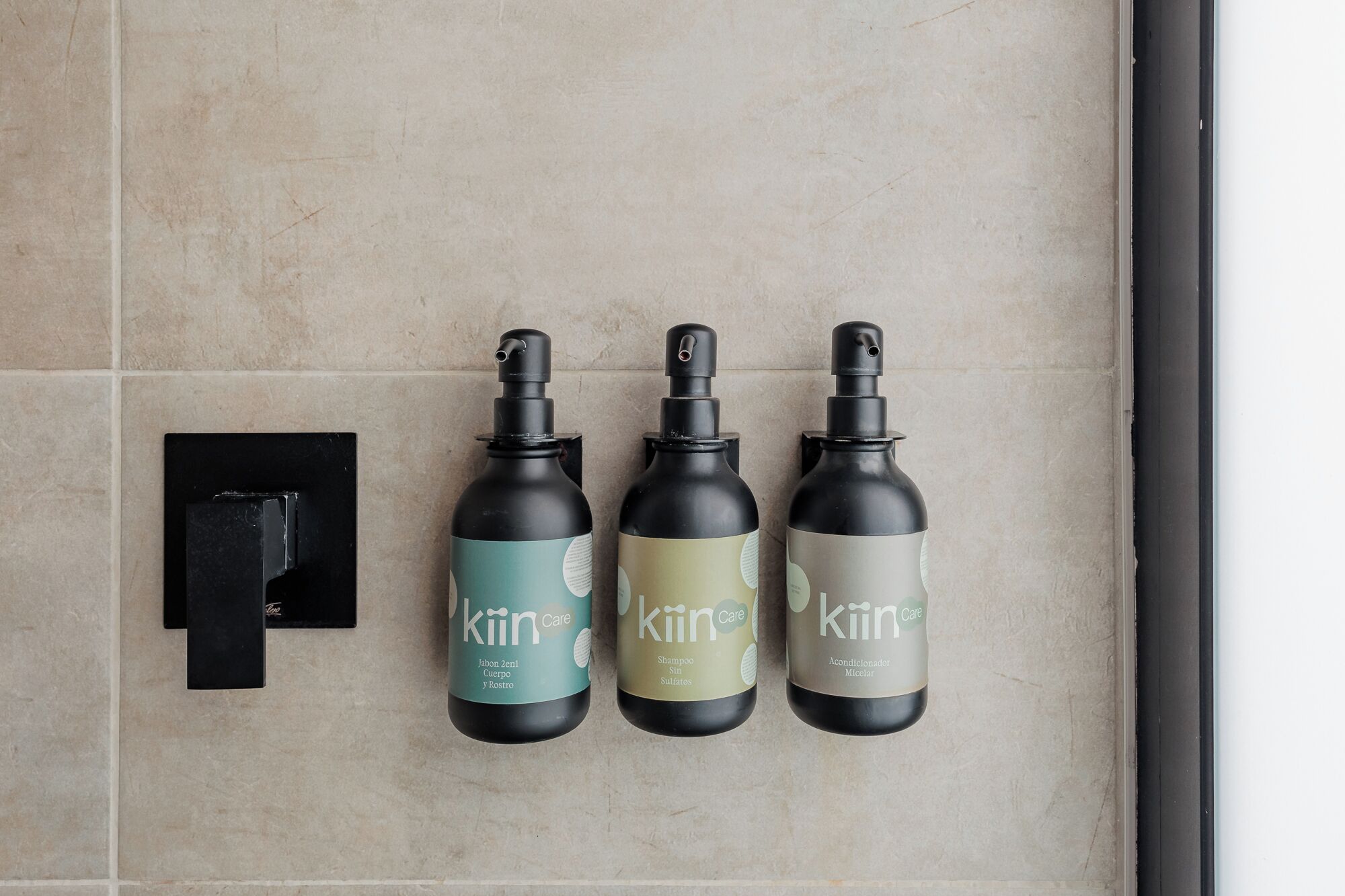 Three bottles of 'kiin Care' shampoo and conditioner on a tiled wall.