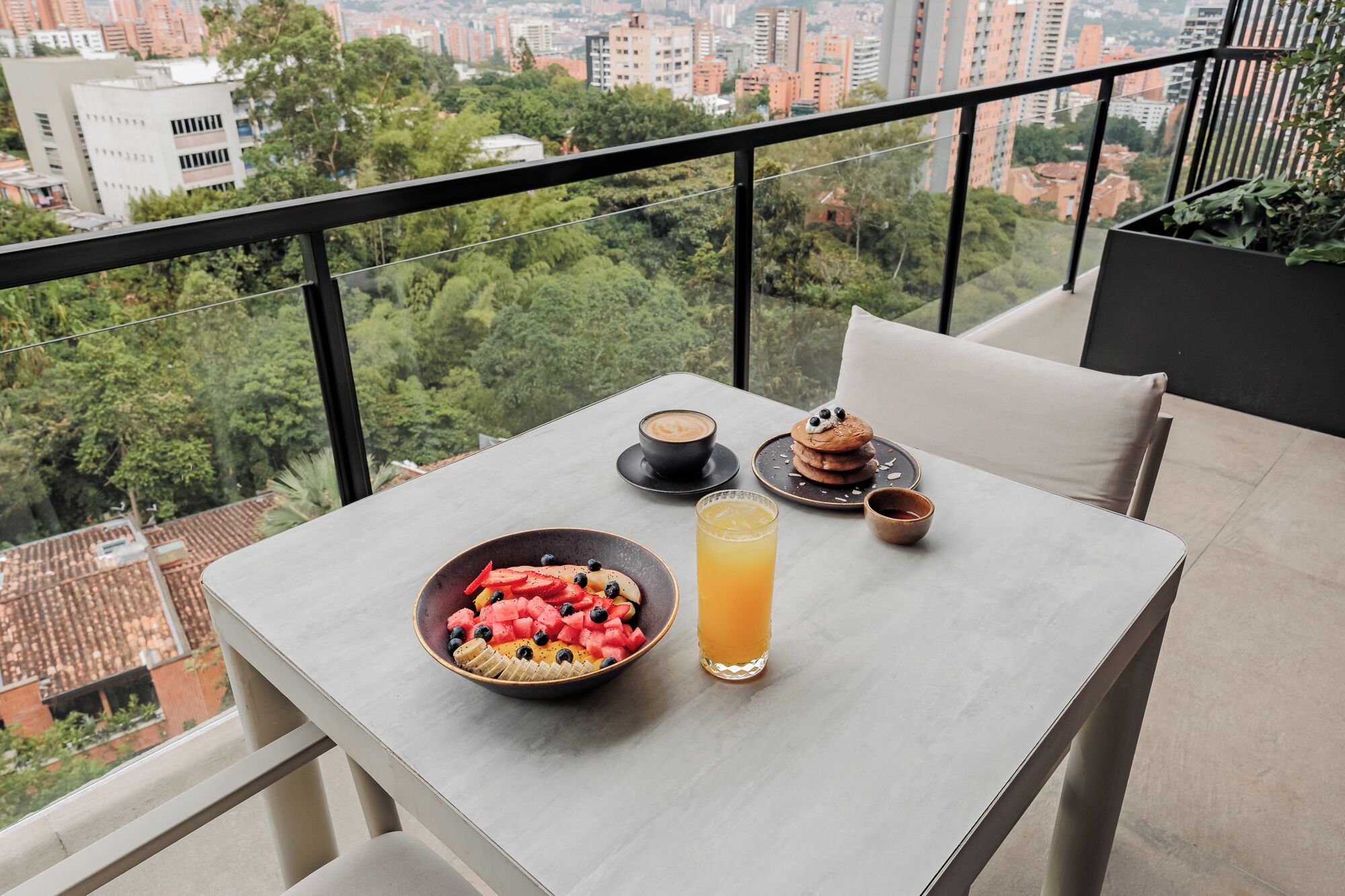 A table with breakfast items, a glass of orange juice, and a view of a cityscape.
