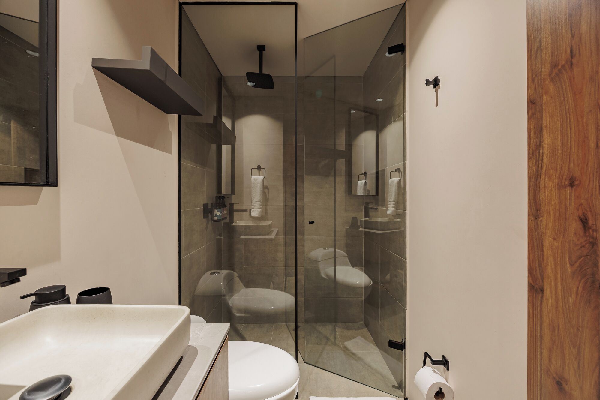 Een moderne badkamer met een douchecabine van glas, een wit wastafelmeubel en een houten deur.
