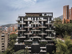 A multi-story building with balconies, a rooftop garden, and a view of surrounding urban area. - Kiin Living- "Child-free coliving" (Medellín)