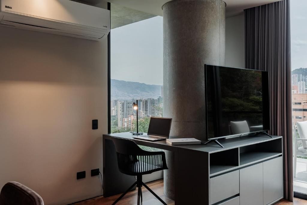 A modern room with a large window, a flat-screen TV, a desk, and a chair.