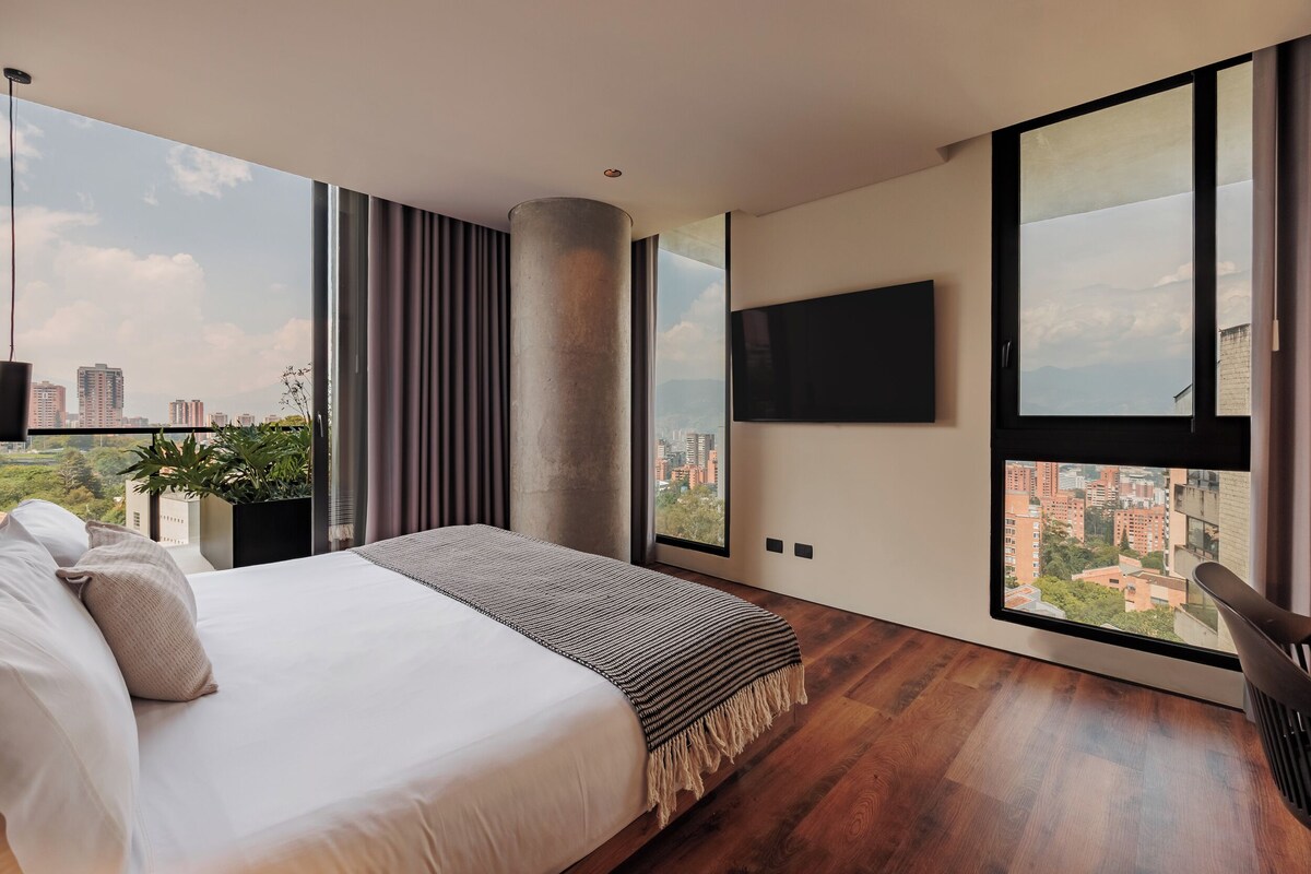 Una camera da letto moderna con un letto grande, una TV a parete e vista sulla città attraverso ampie finestre.