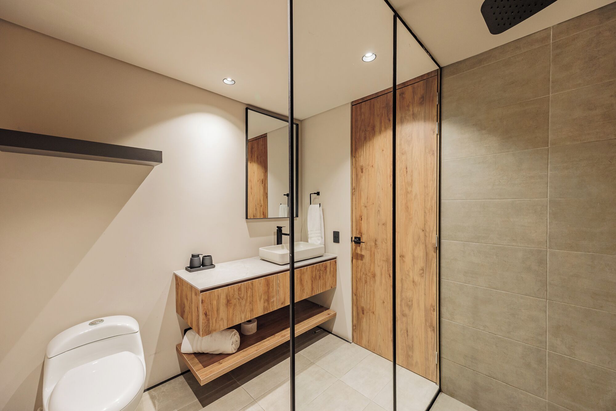 A modern bathroom with a wooden vanity, a toilet, and a shower area.