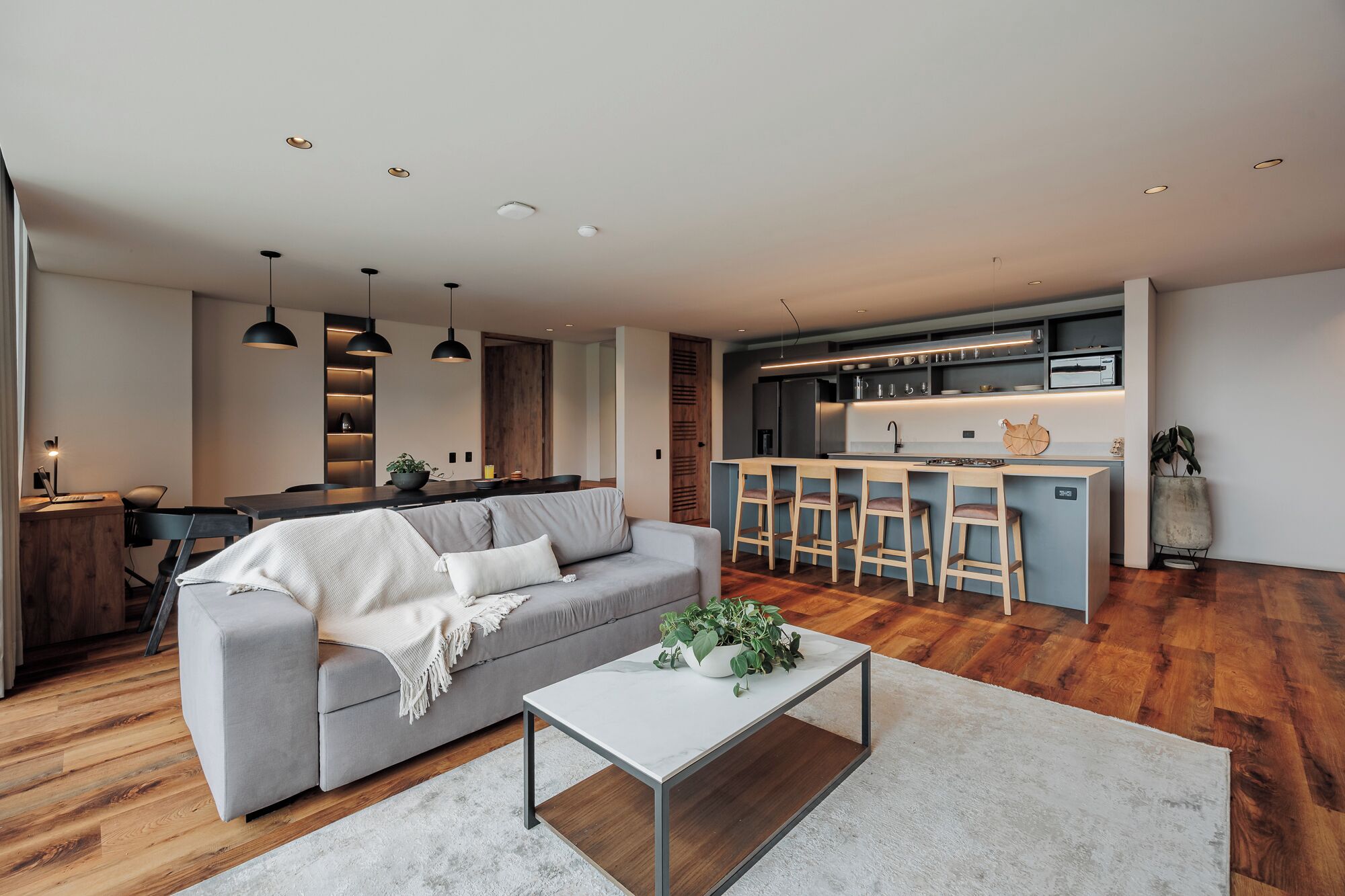 A modern living room with a grey sofa, a coffee table, and a kitchen area with a bar.