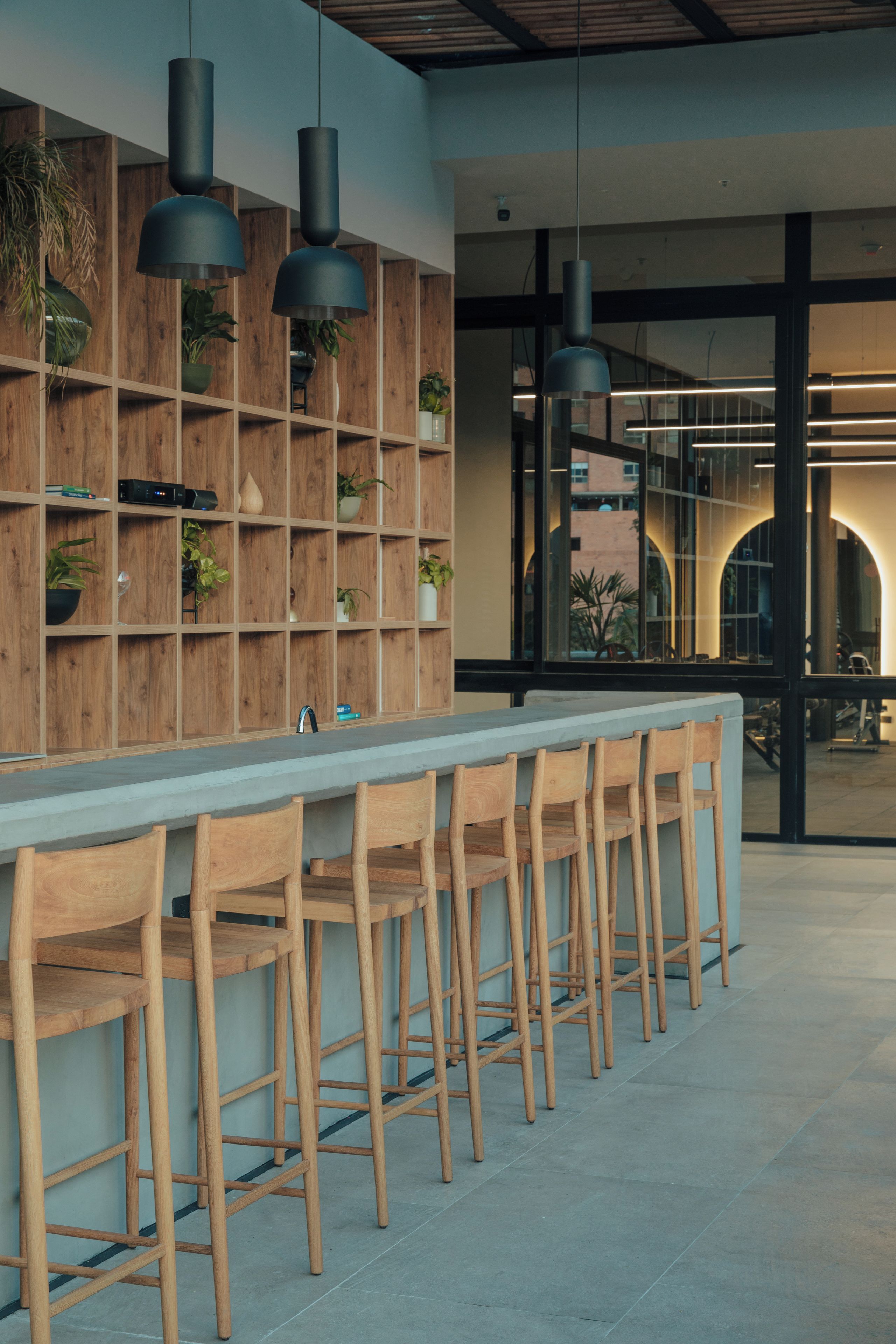 Un espace bar moderne avec des étagères en bois, des plantes en pot et un long comptoir agrémenté de chaises en bois.