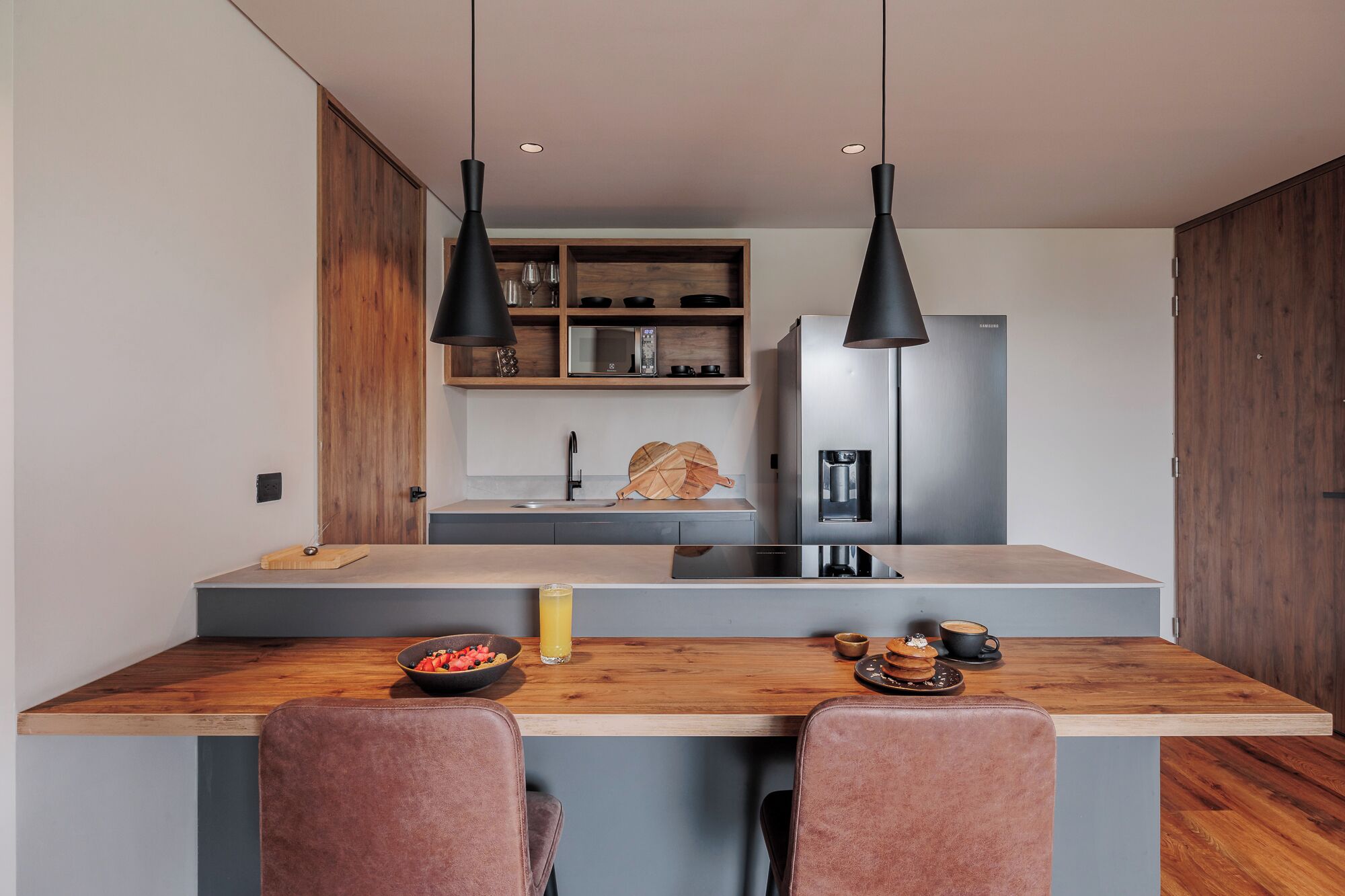 A modern kitchen with a central island, two pendant lights, a built-in microwave, and a refrigerator.
