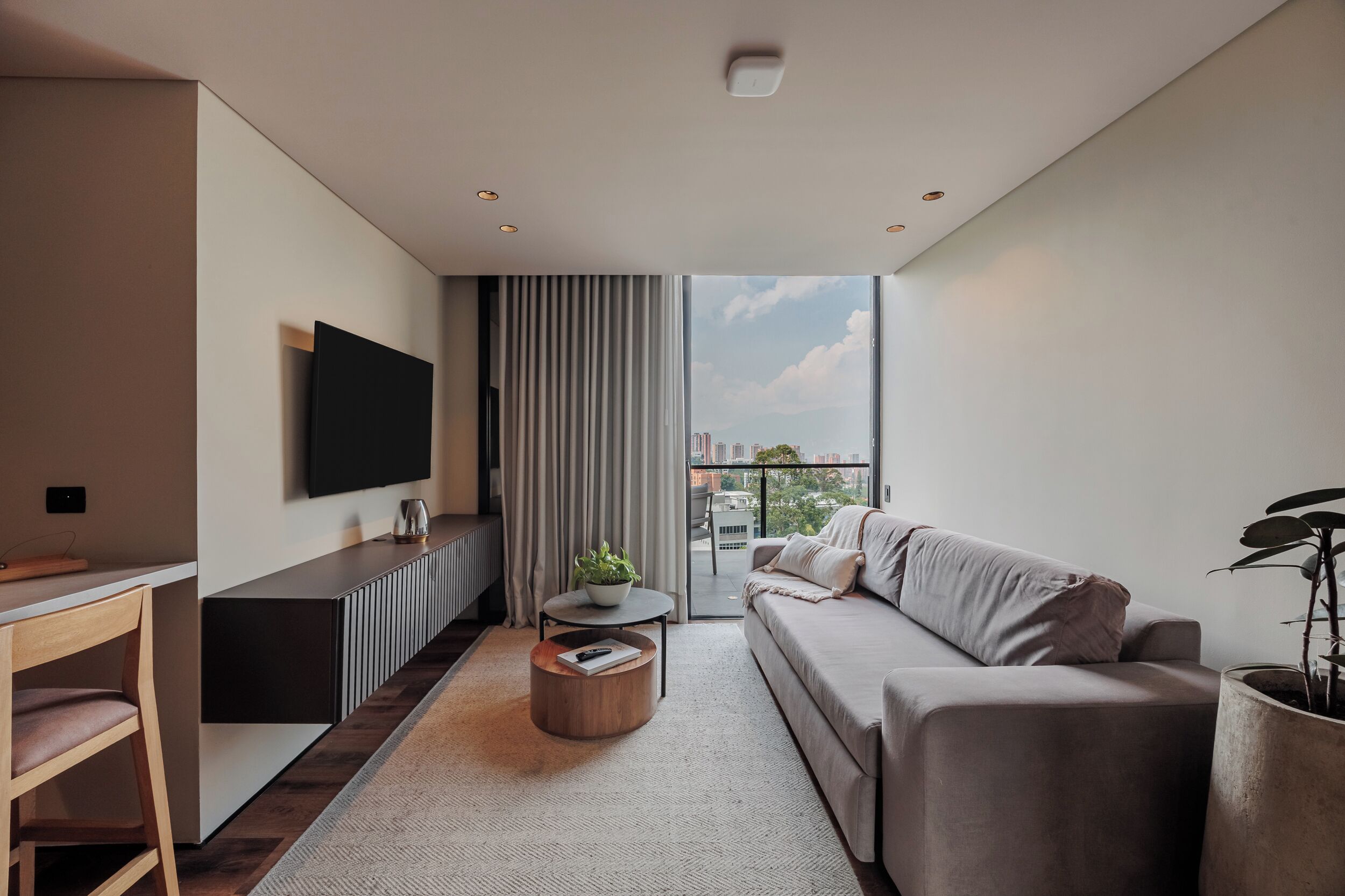 Un soggiorno moderno con un divano, un tavolino, una TV a parete e un'ampia finestra con vista sulla città.