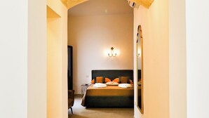 Un pasillo que conduce a un dormitorio con cama, una lámpara de pared y un espejo.