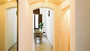 Un pasillo con un muro espejado, un comedor con sillas y una mesa, y una lámpara en el techo.