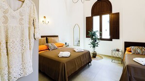 Un dormitorio con dos camas, un candelabro, un espejo, una ventana con contraventanas y un perchero.