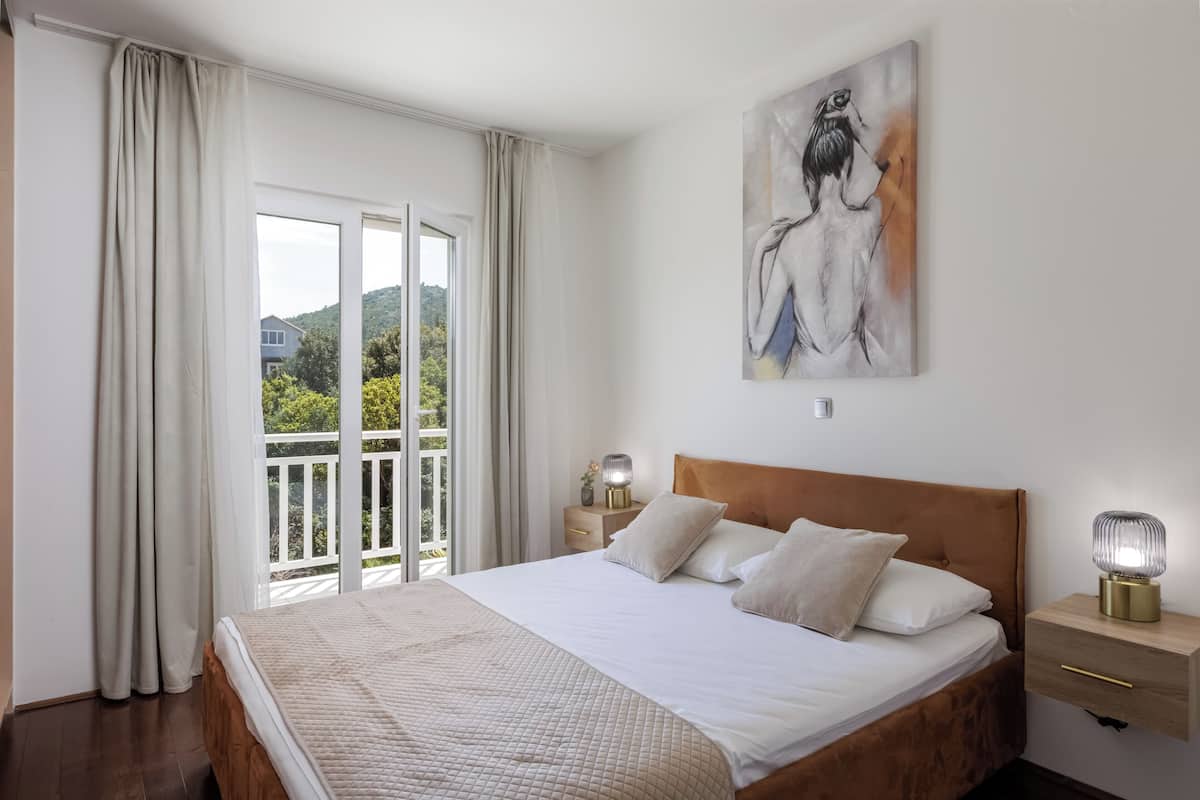 A bedroom with a large bed, a nightstand, a lamp, and a painting on the wall.
