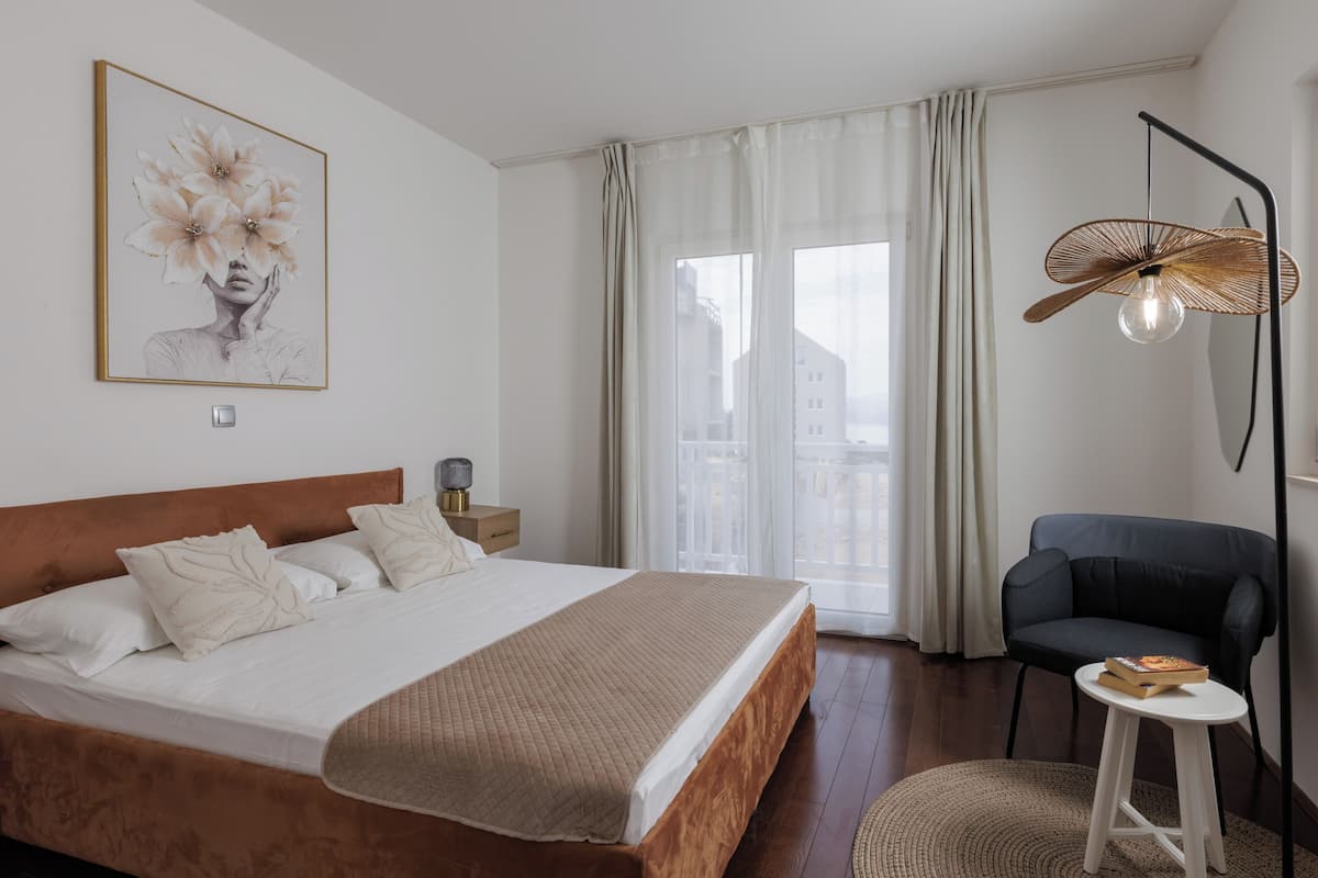 A bedroom with a bed, a chair, a bedside table, a lamp, and a window with curtains.