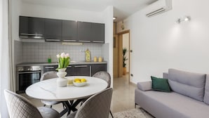 A modern kitchen with grey cabinets, a white dining table with chairs, and a grey sofa in the living area. - Apartments Villa Olea Solis (Cavtat)