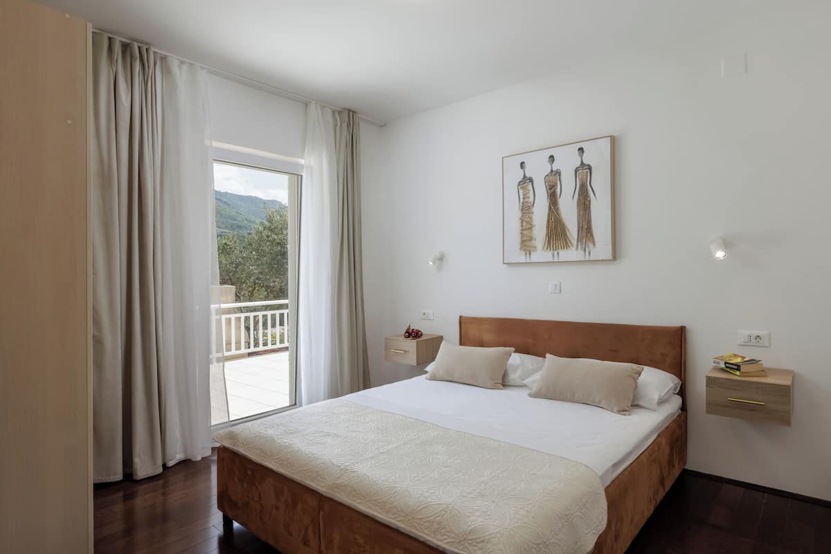 Un dormitorio con una cama grande, una mesita de noche, una estantería en la pared y una ventana con cortinas.