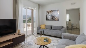 A modern living room with a flat-screen TV, grey sofas, a coffee table, and a painting on the wall. - Apartments Villa Olea Solis (Cavtat)