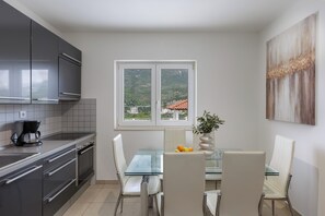 Eine moderne Küche mit Essbereich, einem großen Fenster und Blick auf ein Gebäude mit rotem Dach.