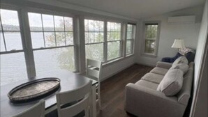 Een kamer met een eettafel, stoelen, een bank en grote ramen met uitzicht op een wateroppervlak.