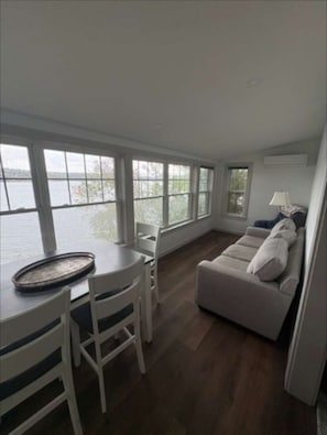 Ein Zimmer mit Esstisch, Stühlen, einer Couch und großen Fenstern mit Blick auf ein Gewässer.