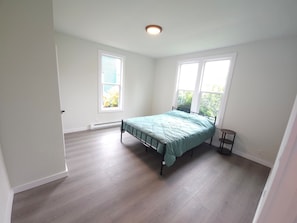 Une chambre à coucher avec un lit, deux fenêtres, un radiateur et une petite table.