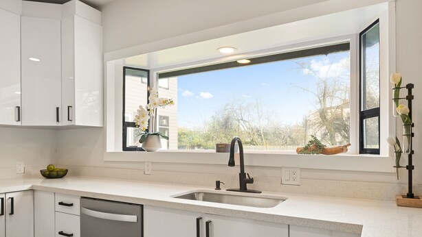 A modern kitchen with white cabinetry, a stainless steel sink, and a window with a view of trees and buildings. - Beautiful 3-bedroom house in wonderful Bellingham for your getaway (Bellingham)