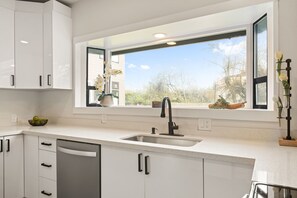 A modern kitchen with white cabinetry, a stainless steel sink, and a window with a view of trees and buildings.
