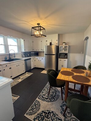 Eine moderne Küche mit weißen Schränken, einem Edelstahlkühlschrank, einem eingebauten Backofen und einem Essbereich mit Holztisch und Stühlen.