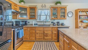 A kitchen with wooden cabinets, a stove, a microwave, and a sink. - Charming 3-bedroom cottage with AC in Jamaica Beach (Jamaica Beach)