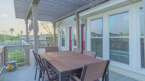 A covered outdoor deck with a wooden table and chairs, large windows with blinds, and a view of the surrounding area. - Charming 3-bedroom cottage with AC in Jamaica Beach (Jamaica Beach)